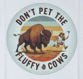 A white short-sleeve crewneck t-shirt. The shirt features a circular graphic in the center with a bison, a tourist, and the text 'DON'T PET THE FLUFFY COWS'.