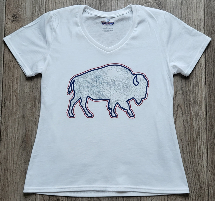 A white women's short-sleeve V-neck t-shirt featuring a graphic of a bison outline filled with a map pattern and outlined in red and blue, laid flat on a gray wood plank background.