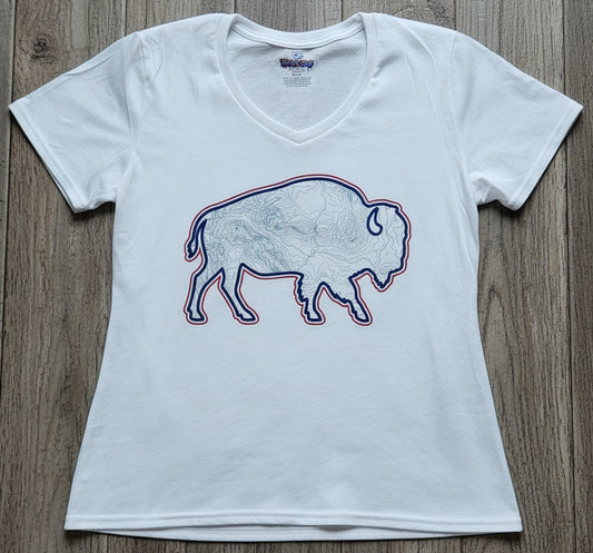 A white women's short-sleeve V-neck t-shirt featuring a graphic of a bison outline filled with a map pattern and outlined in red and blue, laid flat on a gray wood plank background.