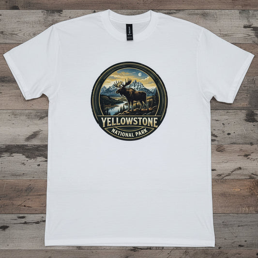 A white short-sleeve crewneck t-shirt laid flat on a rustic wooden plank background. The center of the shirt features a circular graphic print depicting a moose in Yellowstone National Park with the text 'YELLOWSTONE NATIONAL PARK' below it.