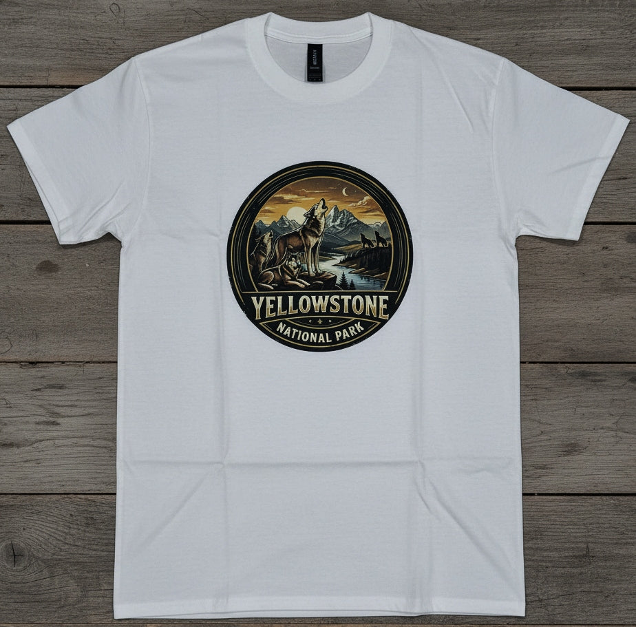 A white short-sleeve crewneck t-shirt laid flat on a rustic gray-brown wooden plank background. The center of the shirt features a circular graphic print depicting a Wolf in Yellowstone National Park, with 'YELLOWSTONE NATIONAL PARK' printed below the illustration.