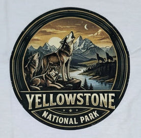 A white short-sleeve crewneck t-shirt laid flat on a rustic wooden plank background. The center of the shirt features a circular graphic print depicting a Yellowstone National Park scene with a wolf, mountains, and a sunset, with the text 'YELLOWSTONE NATIONAL PARK' printed below.
