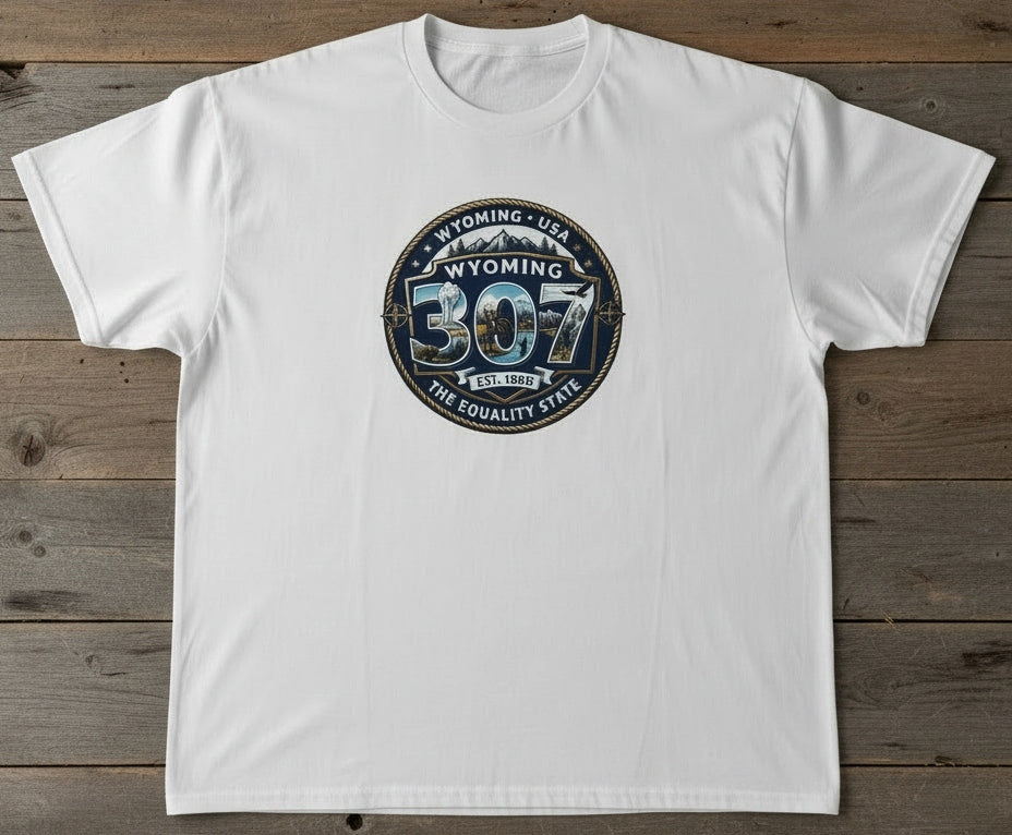 A white short-sleeve crewneck t-shirt laid flat on a rustic dark wood background, featuring a circular graphic on the chest with the text 'WYOMING 307 THE EQUALITY STATE'.