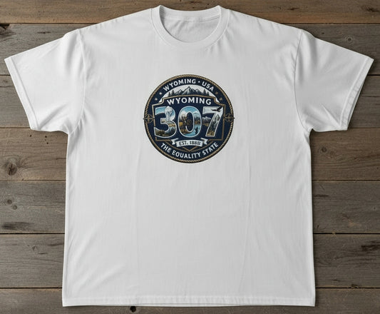A white short-sleeve crewneck t-shirt laid flat on a rustic dark wood background, featuring a circular graphic on the chest with the text 'WYOMING 307 THE EQUALITY STATE'.