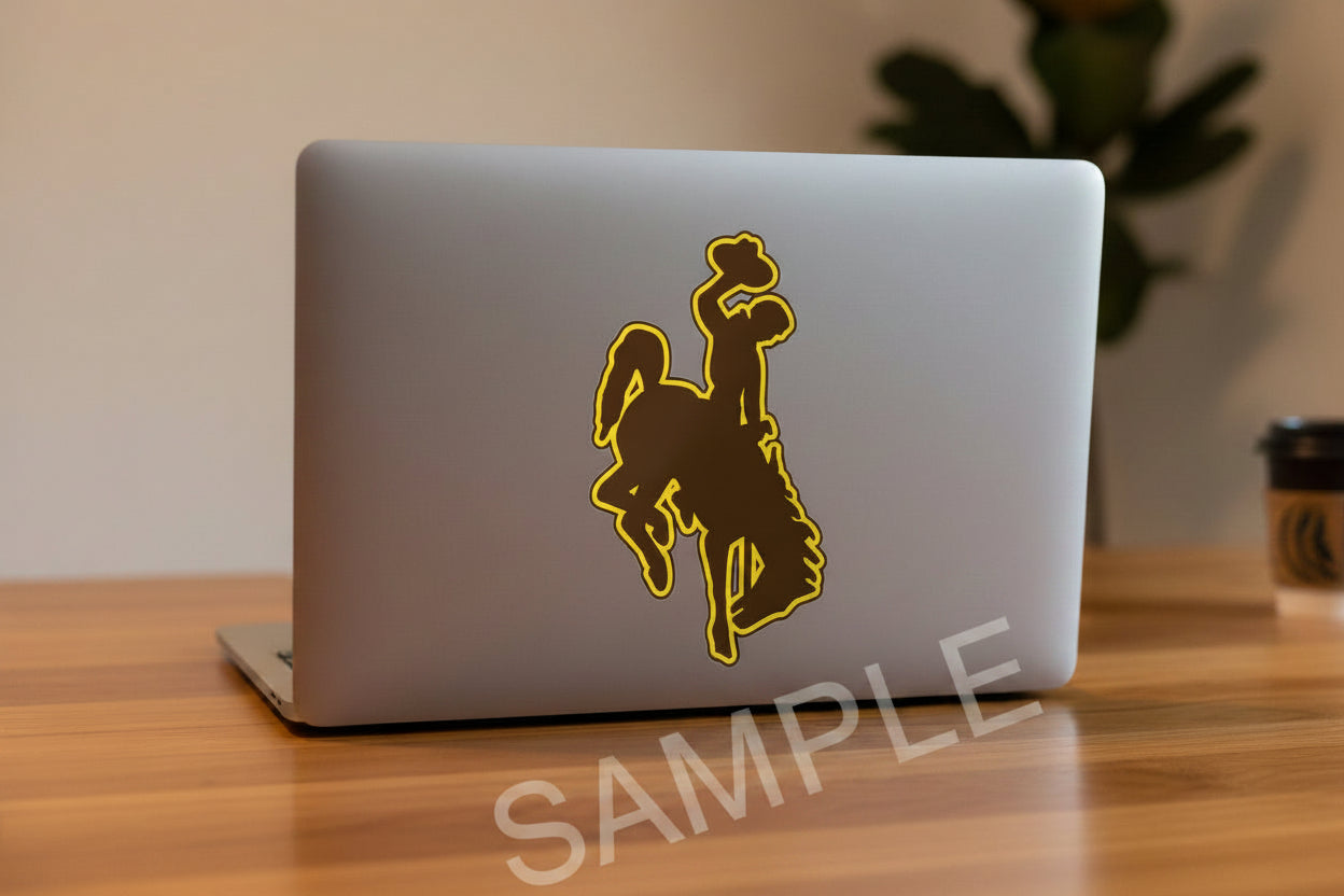 University of Wyoming Bucking Horse logo Sticker featuring a dark brown silhouette of a cowboy riding a bucking horse, outlined in bright yellow, shown on a light gray laptop.
