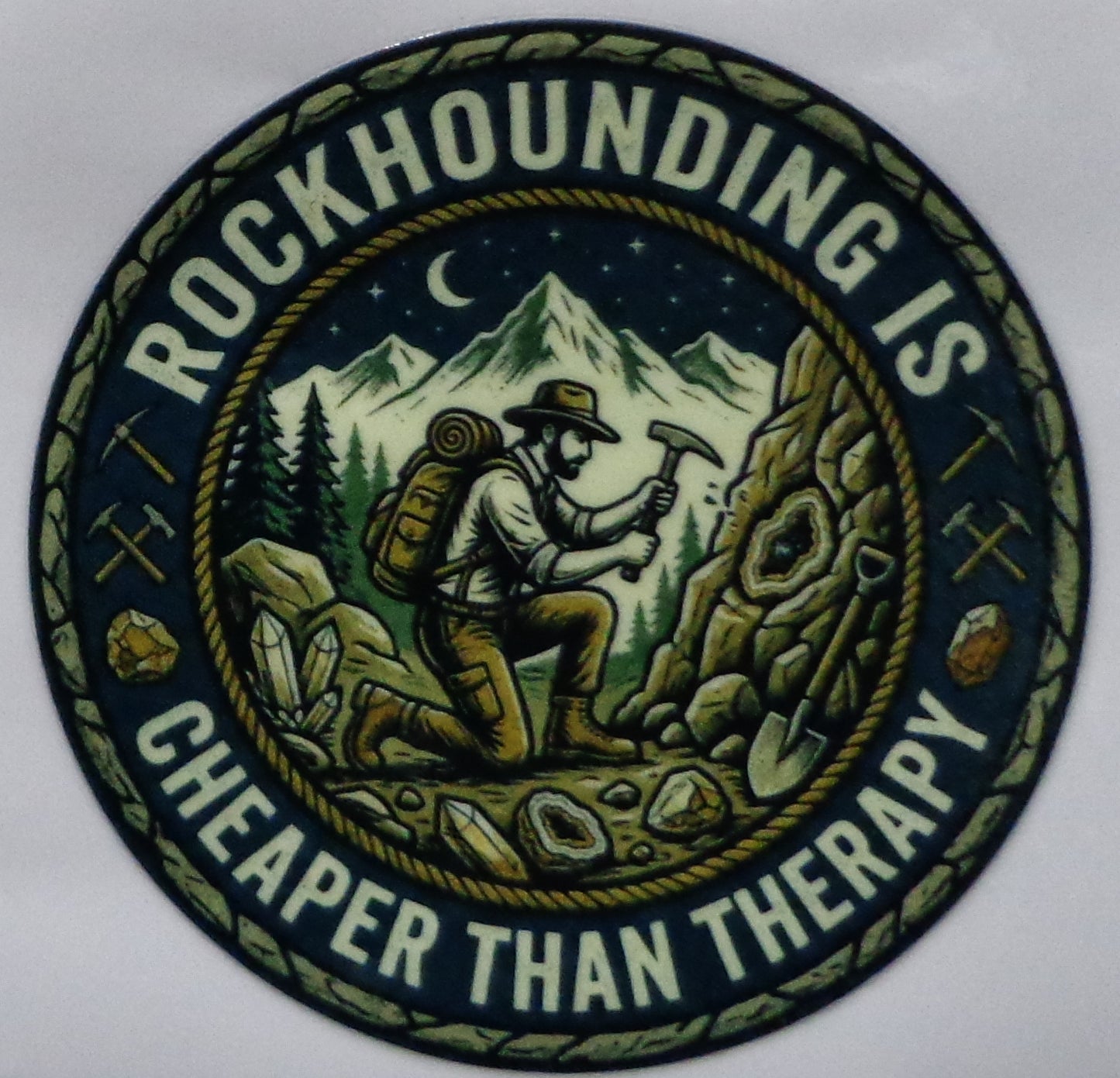 Circular sticker with a mountain scene and text 'Rockhounding is cheaper than therapy' on a white background.