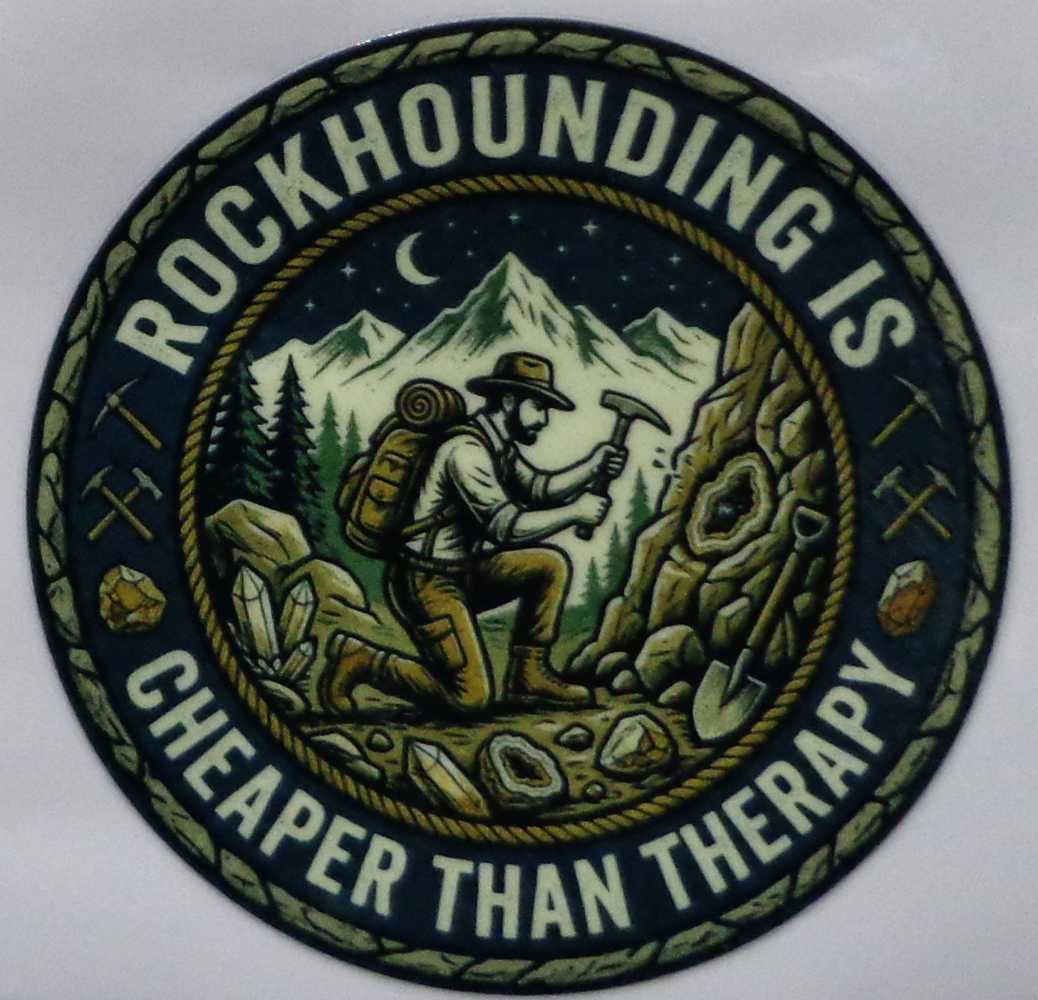 Circular sticker with a mountain scene and text 'Rockhounding is cheaper than therapy' on a white background.