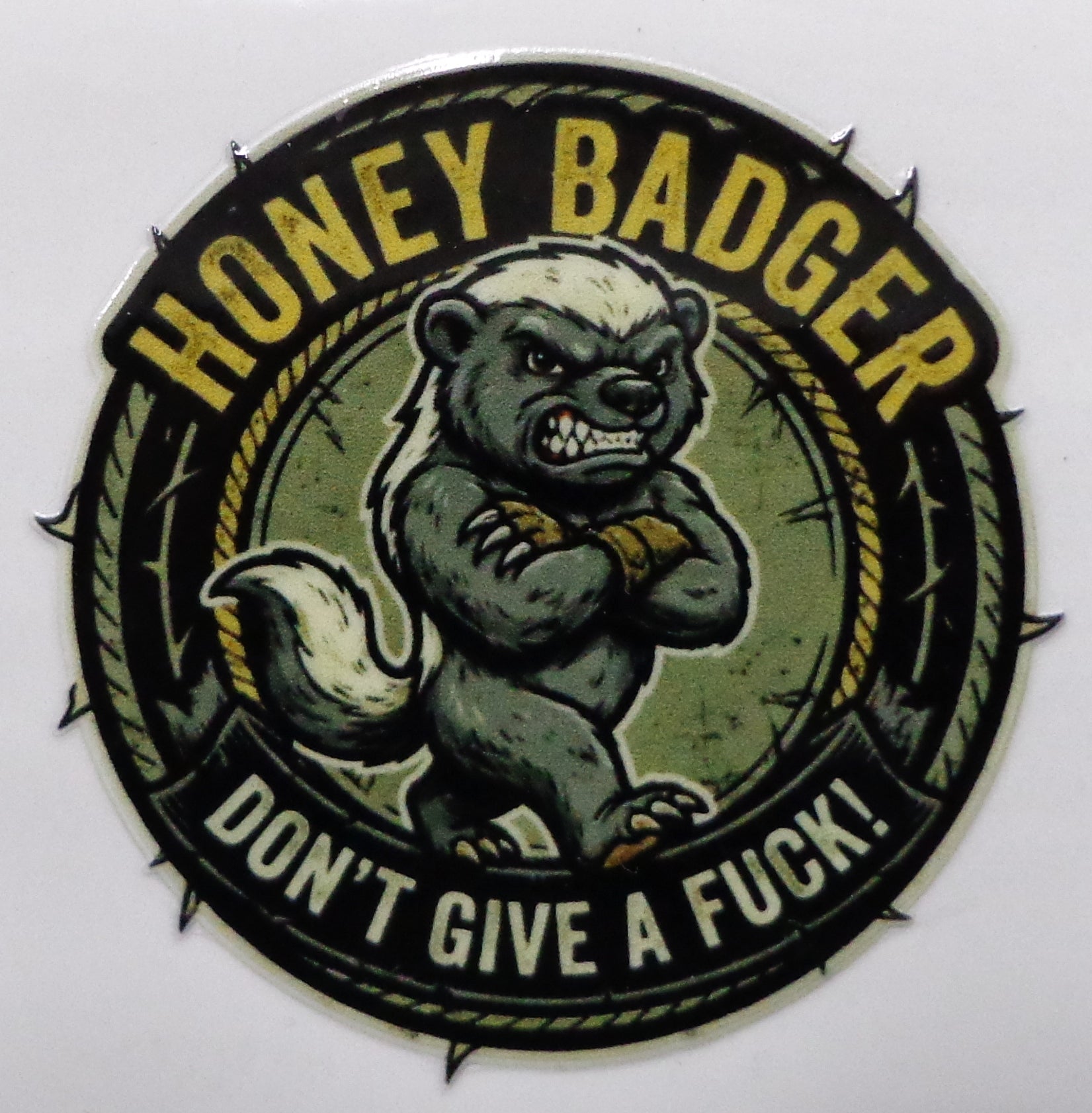 A circular sticker or patch featuring a cartoon honey badger with the text 'HONEY BADGER' at the top and 'DON'T GIVE A FUCK!' at the bottom, shown on a plain light background.