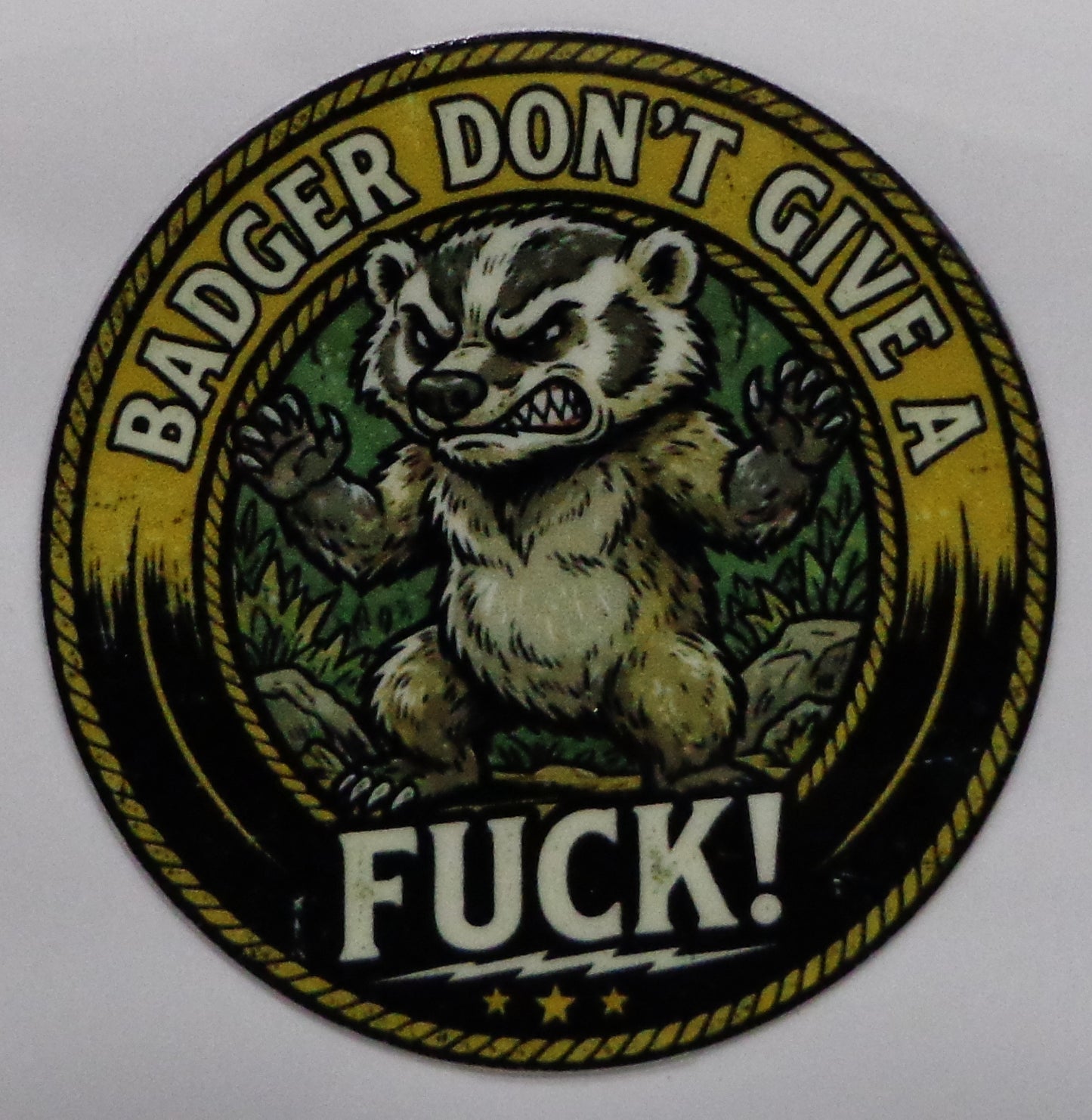 A circular sticker featuring a grumpy badger with raised paws, surrounded by the text 'BADGER DON'T GIVE A FUCK!' in white lettering on a yellow and black background.