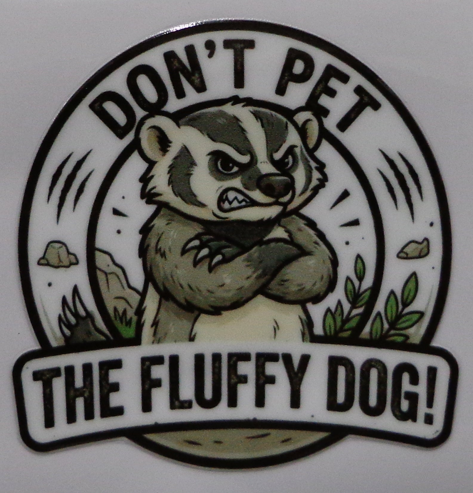A circular sticker or decal featuring a cartoon badger with crossed arms and the text 'DON'T PET THE FLUFFY DOG!' on a plain light background.