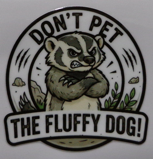 A circular sticker or decal featuring a cartoon badger with crossed arms and the text 'DON'T PET THE FLUFFY DOG!' on a plain light background.