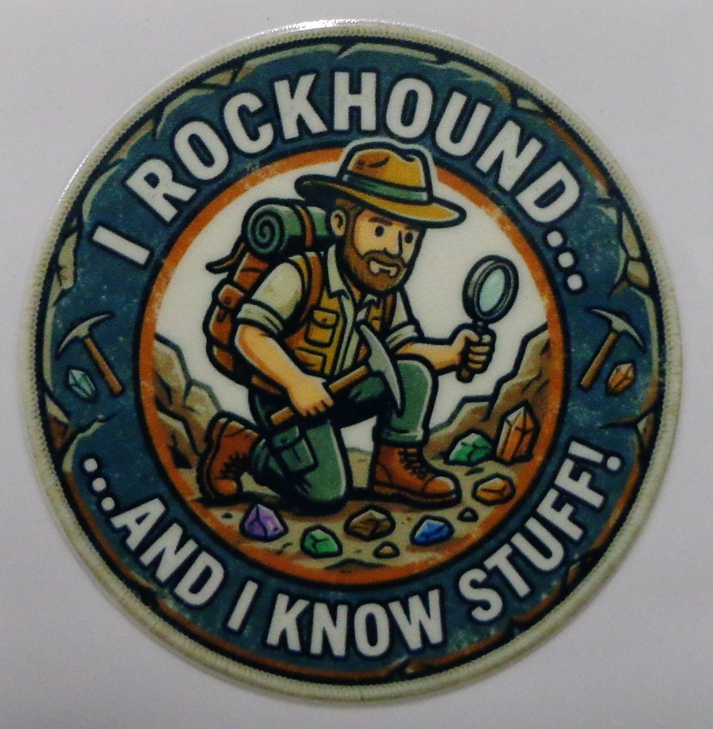 A circular novelty sticker featuring a cartoon rockhound explorer with a backpack, hat, and magnifying glass, surrounded by the text 'I ROCKHOUND... ....AND I KNOW STUFF.