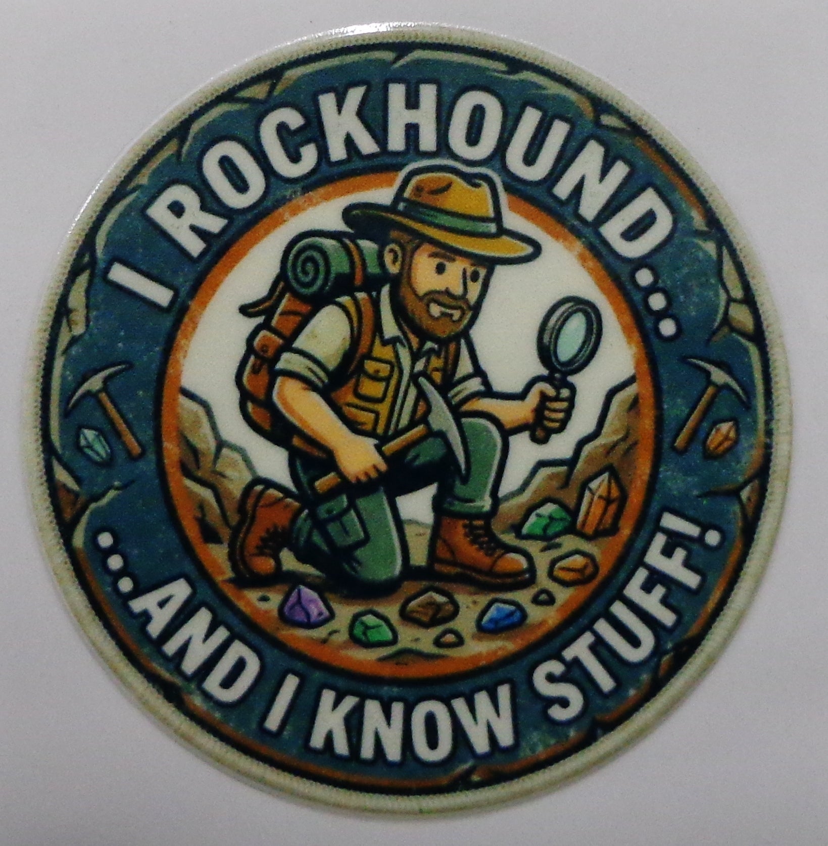 A circular novelty sticker featuring a cartoon rockhound explorer with a backpack, hat, and magnifying glass, surrounded by the text 'I ROCKHOUND... ....AND I KNOW STUFF.
