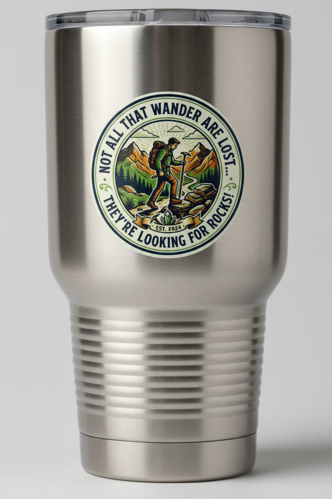 A circular vintage-style sticker or decal featuring a hiking man with a backpack and trekking pole in front of mountains, with the text 'NOT ALL THAT WANDER ARE LOST... THEY'RE LOOKING FOR ROCKS. On a stainless steel tumblr. 