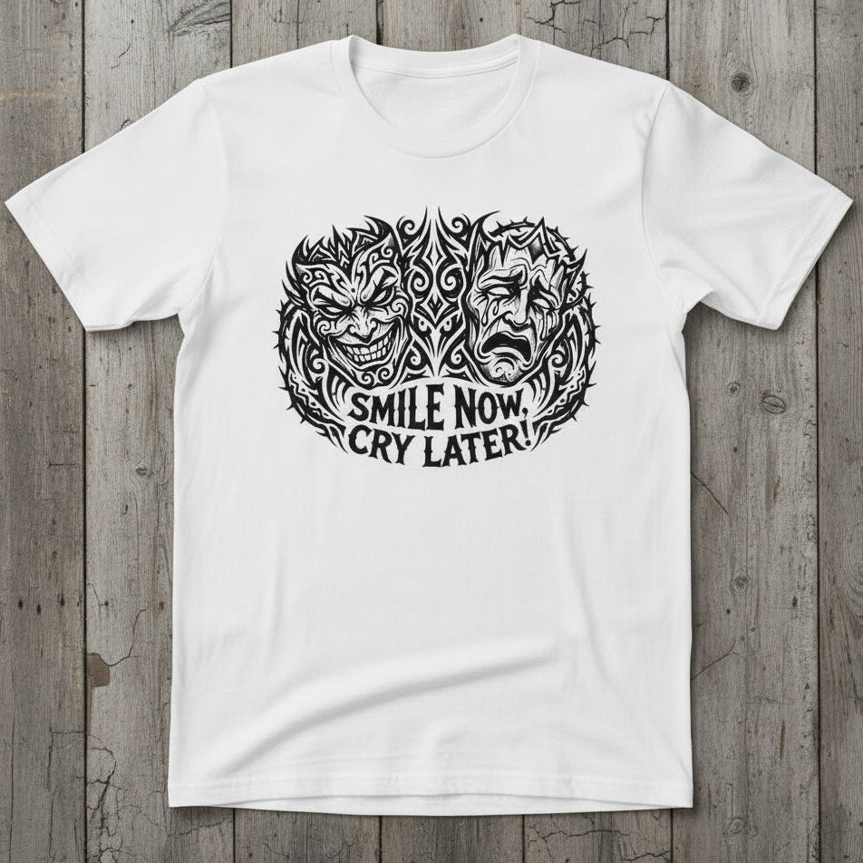 A white short-sleeve t-shirt laid flat on a wood background, featuring a black graphic print of a split face with the text 'SMILE NOW CRY LATER!' underneath.