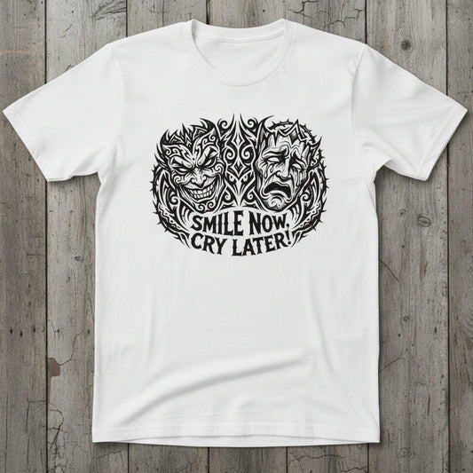 A white short-sleeve t-shirt laid flat on a wood background, featuring a black graphic print of a split face with the text 'SMILE NOW CRY LATER!' underneath.